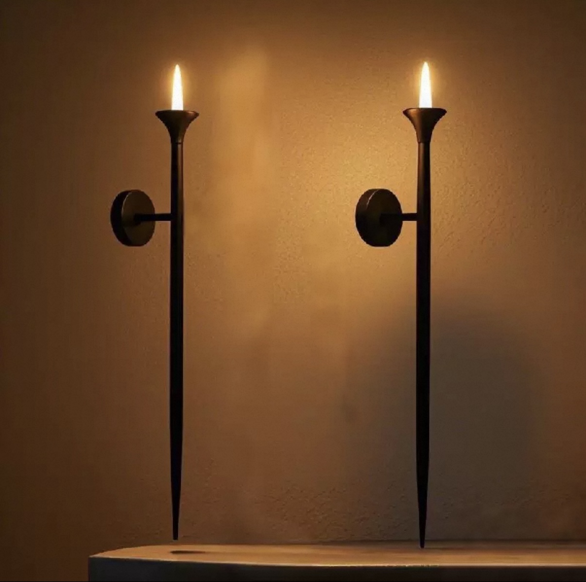 Tall black wall-mounted taper candle holders casting warm light